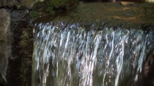 Slow motion, close up shot of a small waterfall with water falling down over some rocks