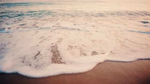 Close up of small ocean waves gently rolling onto the sandy beach at sunset