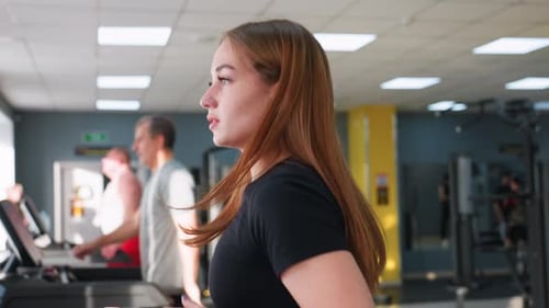 Close Up of Focused Woman Running on Treadmill in Gym with Other People Exercising