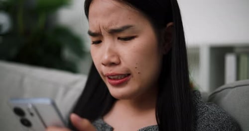 Worried Woman Using Smartphone Indoors on Couch