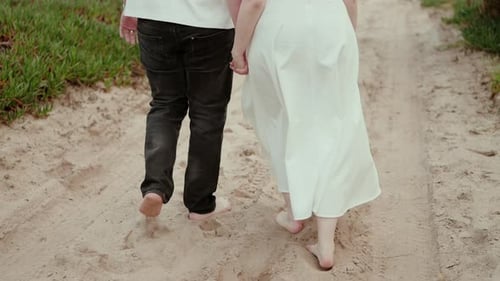 Couple walking barefoot on sandy path holding hands outdoors