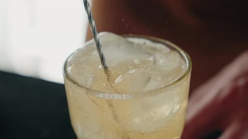 Stirring sparkling drink with ice cubes
