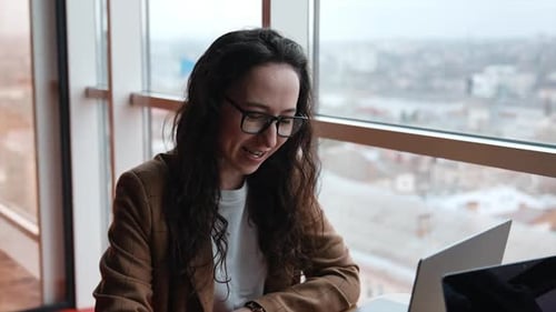 Woman Working on Laptop by City Window