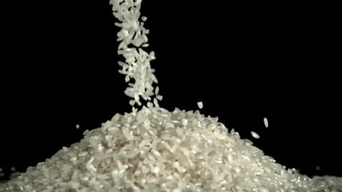 Rice Grains Pouring onto Pile Against Black Backdrop