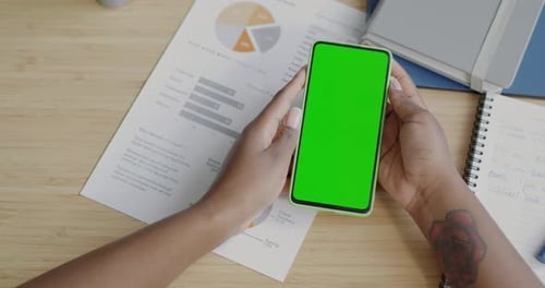 Closeup of Female Hand and Chroma Key Green Screen Smartphone Against Desk Background with Business