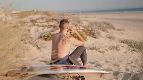 Surfista contempla a próxima onda enquanto está sentado na praia com sua prancha de surfe