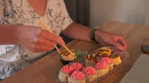 Woman Eating Sushi Rolls with Chopsticks at Table