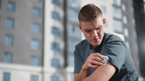 Young Man Placing Nicotine Patch on Upper Arm with Residential Building Behind