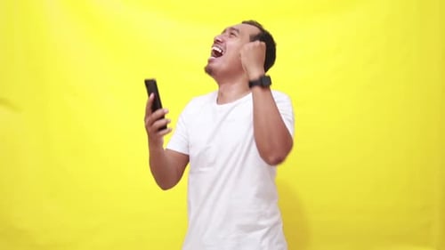 Smartphone, excited with asian man isolated yellow background in studio, celebration and social medi