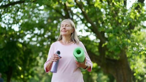 Woman Walking with Yoga Mat in Park