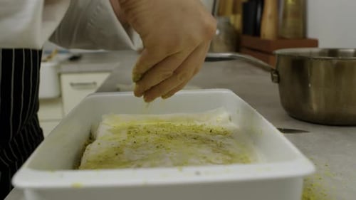 Adding chopped nuts onto baklava dough layer inside ceramic pan.