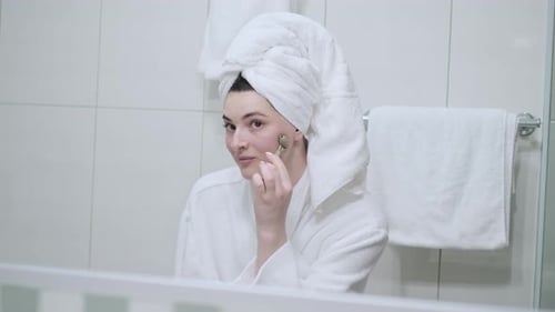 Woman Massaging Face with Beauty Roller in Bathroom