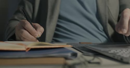Closeup of Male Hands Using Laptop and Writing in Notebook Working at Desk in Office at Night