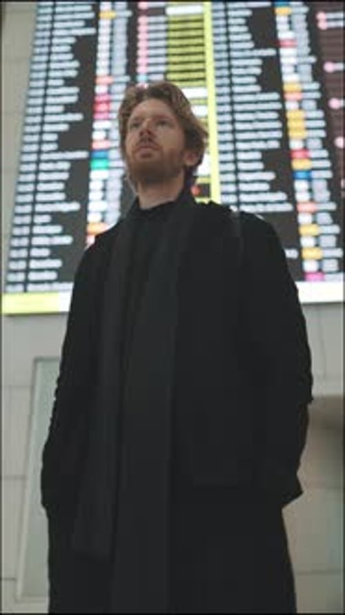 Young Man Checking Flight Departure Board at Airport