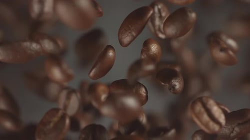 Superzeitlupenaufnahme fallender gerösteter Kaffeebohnen mit Rauch beim Makro-Rösten von fliegendem Kaffee