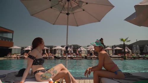Two Beautiful Young Women Talk and Take Pleasure in Their Time Beside the Pool