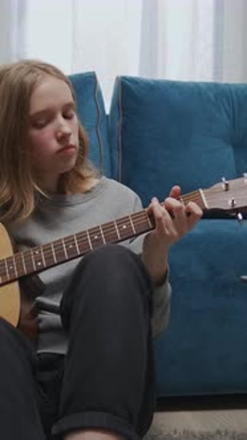 Teen Girl Practicing Acoustic Guitar Seated on Living Room Floor Focused on Chords and Finger