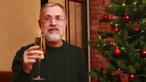an Elderly Man in a Green Knitted Sweater Raising a Toast with Champagne Near the Christmas Tree