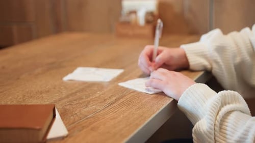 Close Up of Woman Writing Beside Novel on Wooden Table