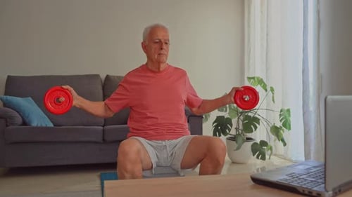 Video of Elderly man exercising with weights at home following watching online tutorial on laptop