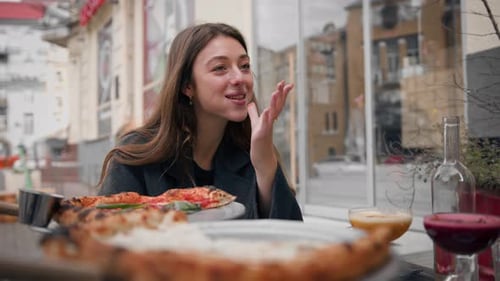 Woman licking fingers on restaurant terrace after eating delicious pizza on date with man