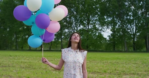 Smiling Woman Holding Balloons in Green Field