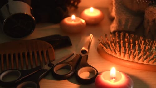 Detalle de herramientas de peluquería, cepillos, tijeras, peines, secador de pelo, toallas, junto a unas velas