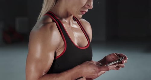Strong Woman Uses Smartphone at the Gym
