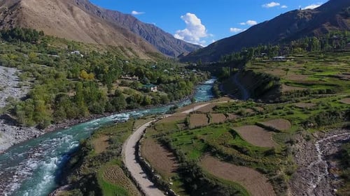 Aerial view of mountains, river, village, road, fields in Pakistan.