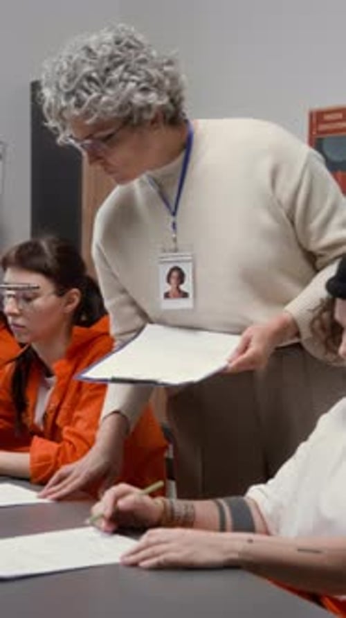 Female Teacher Overseeing Inmates Doing Tests during Class in Prison Vertical