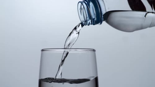 Close Up Of Drinking Water In A Bottle Being Poured Into A Glass On White Background