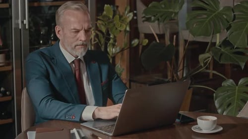Elegant Man Works on Laptop at Table