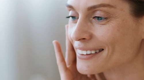 Woman With Fair Skin Applying Skincare Product While Smiling in WellLit Room