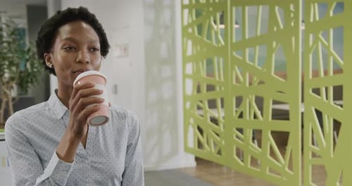 Portrait of happy african american businesswoman drinking takeaway coffee in office, slow motion