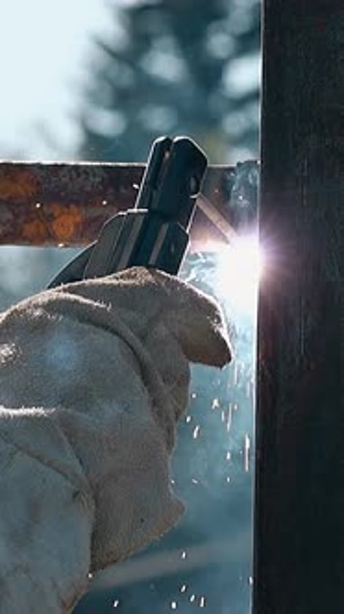 Closeup Worker in Gloves Welds Metal Carcass of Fence