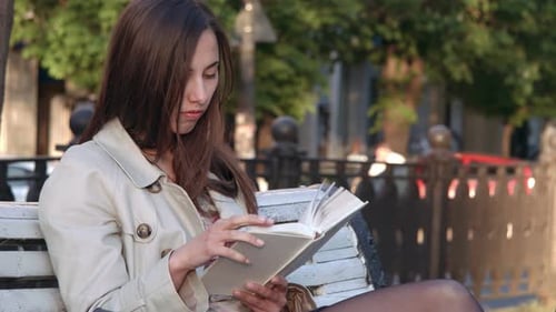 Woman Reads Book on Park Bench in City