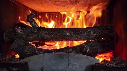 Burning logs in cozy fireplace with vivid flames. Slow-motion and close-up