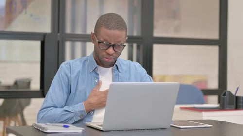 Coughing African Businessman Using Laptop in Office
