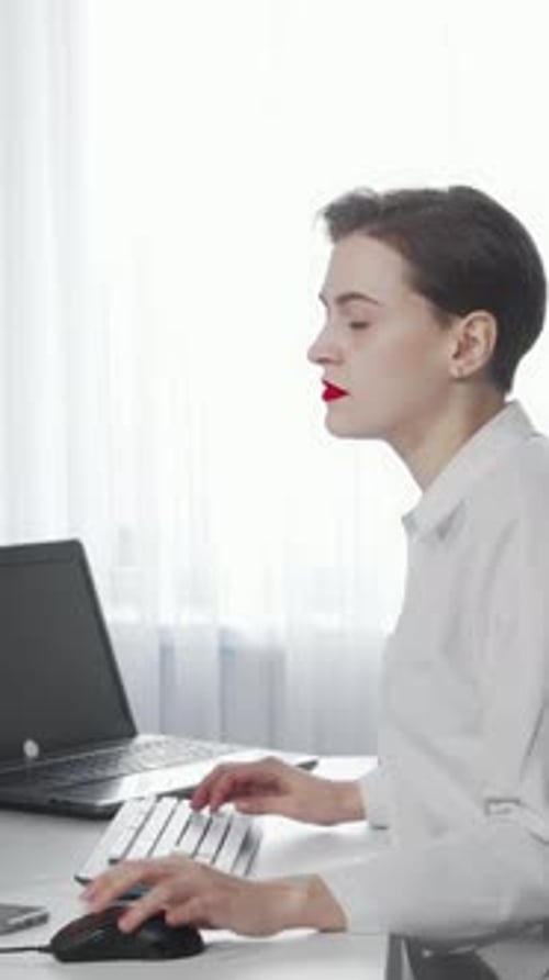 Focused Female Freelancer Multitasking with Smartphone and Laptop in a Bright Office