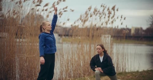 Woman Exercising with Female Friend Against Lake