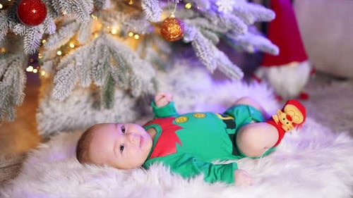 Lovely smiling boy in green elf costume lies on a fluffy plaid.