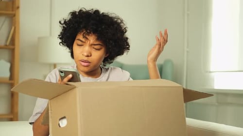 Young Woman Checks Phone with Package Delivery