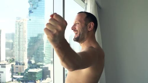 Happy, Successful Man Raising Hands by Window at Home Achievement