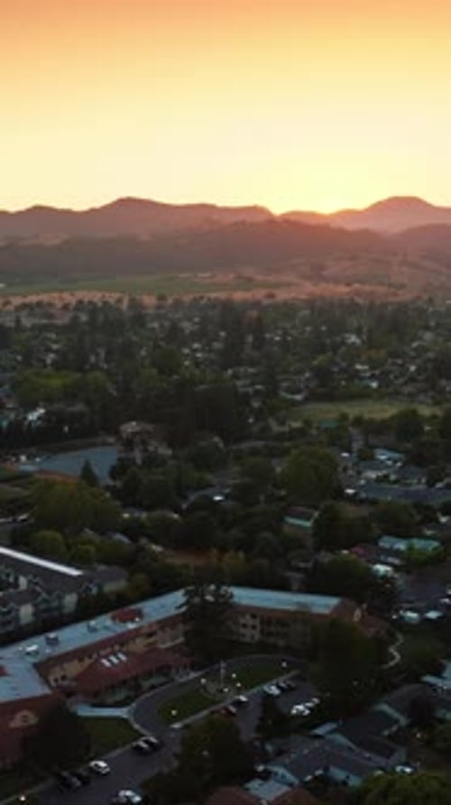 Flying over green city of Napa, California, USA. Mountainous skyline at backdrop of pink skies.