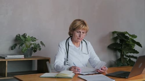 The Doctor is in the Office in a White Coat Glasses and with a Stethoscope