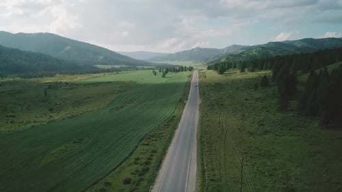 Aerial View of an Asphalt Road in Rural Area Between Green Fields and Hills