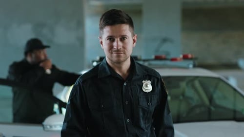 Confident police officer standing with partner near patrol car