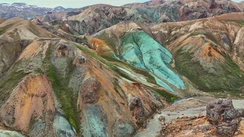 Aerial drone forward view from the left over Grænihryggur, green rock and a glacial river in Landman