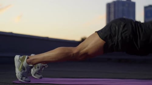 Muscular Man Doing Pushups on Rooftop at Sunset