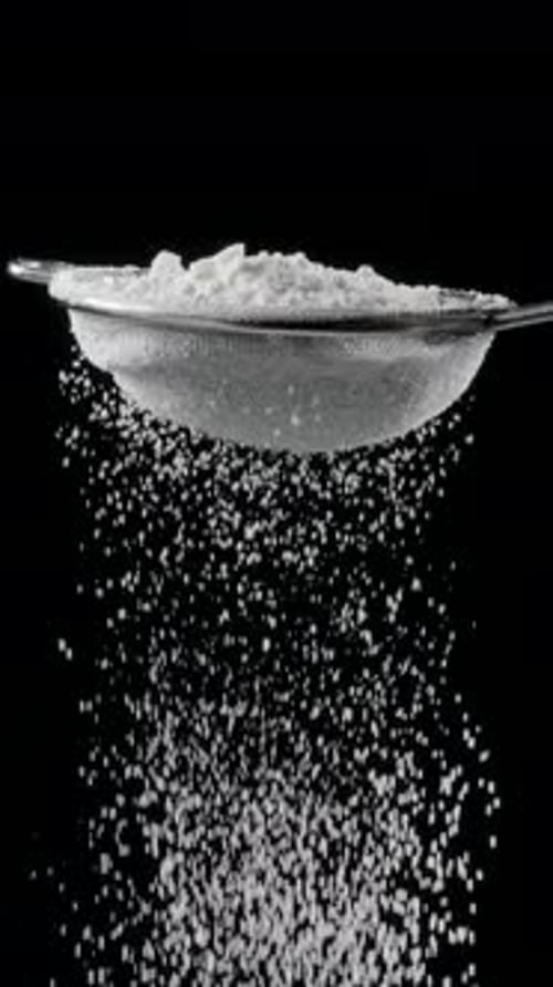 Sift icing sugar or powdered sugar or flour through a sieve tool on black background.